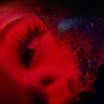 An image of a woman's eye, illuminated in red, looking sadly at something off camera