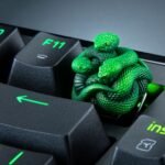 A green snake figurine keycap rising above a mechanical keyboard, replacing the standard F12 key.