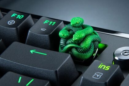 A green snake figurine keycap rising above a mechanical keyboard, replacing the standard F12 key.
