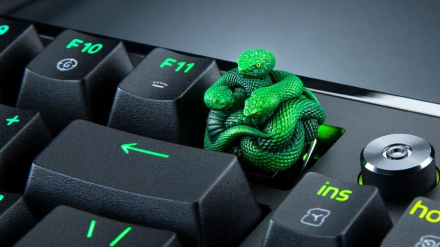 A green snake figurine keycap rising above a mechanical keyboard, replacing the standard F12 key.
